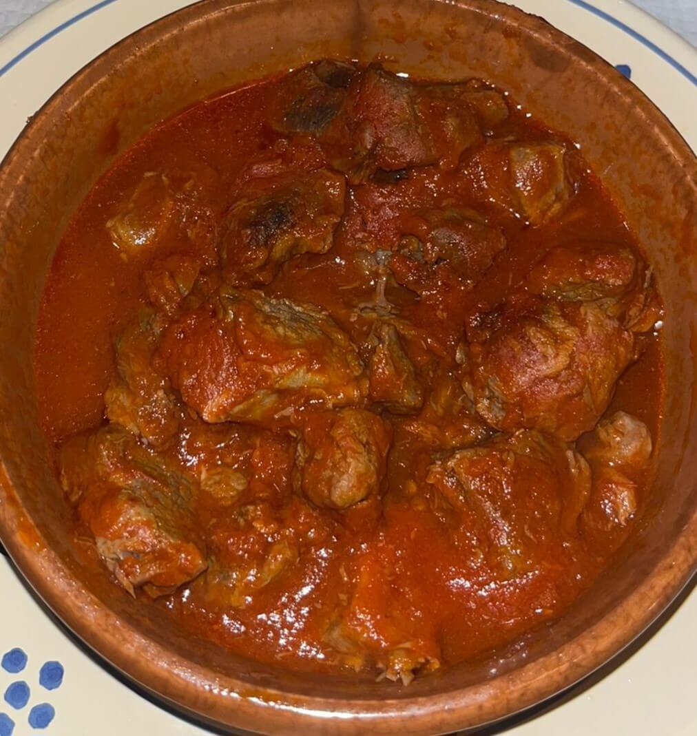 Pezzetti di cavallo al sugo di pomodoro serviti fumanti nella pignata di terracotta, dentro un piatto di ceramica a fiori blu